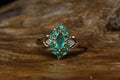 Vintage 9ct yellow gold ring featuring a marquise cut emerald centre stone surrounded by round emeralds in a diamond shape cluster setting with diamond shoulder accents, resting on rustic wood