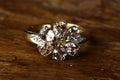 Vintage 9ct yellow gold floral ring featuring pear cut pale pink morganite stones arranged in a flower pattern with diamond accents on the shoulders, resting on rustic wood